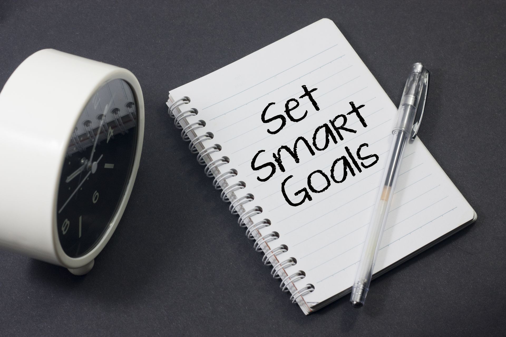 alarm clock,pens and notebook written st smart goals over black background